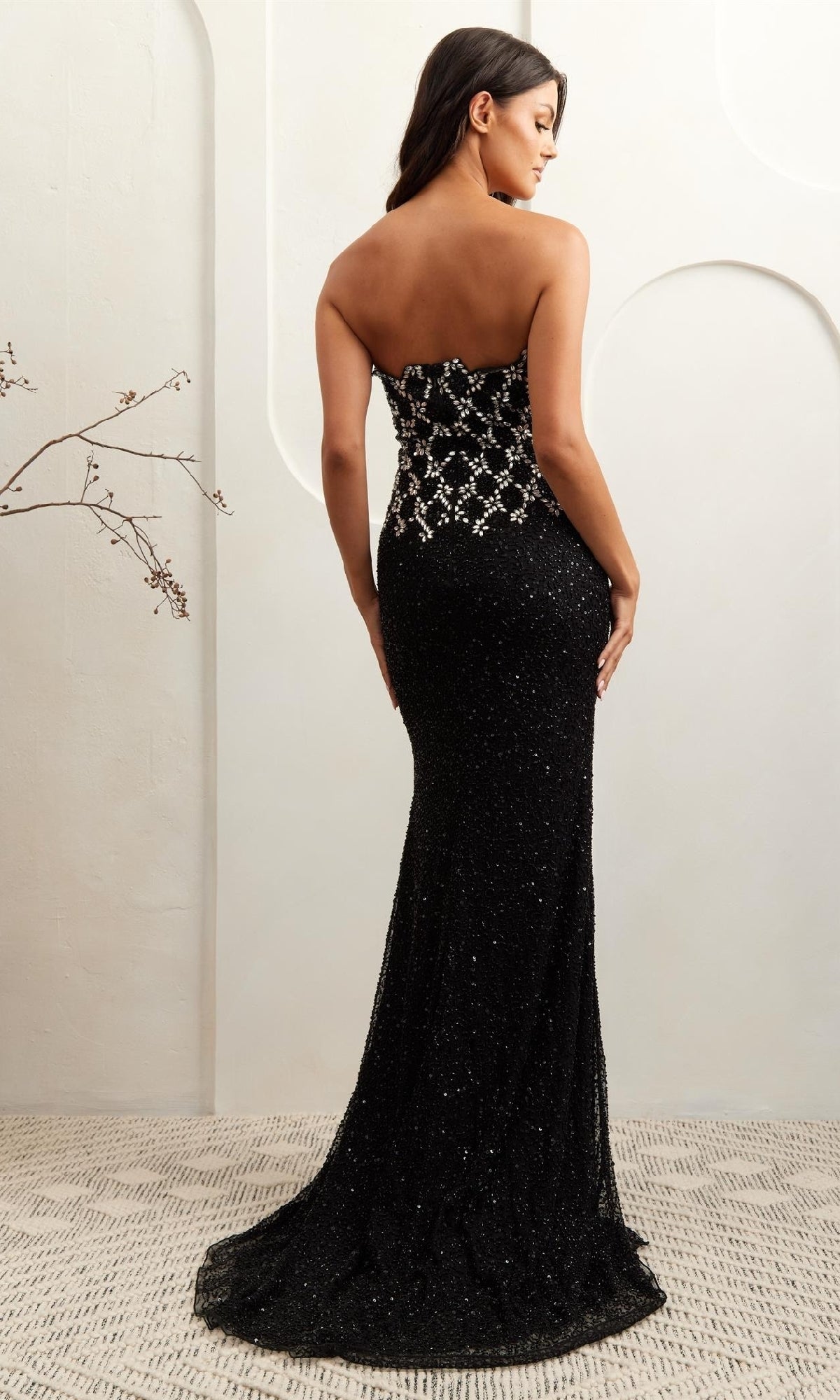 Woman modeling the back of a black sequin evening gown standing in a neutral colored room.